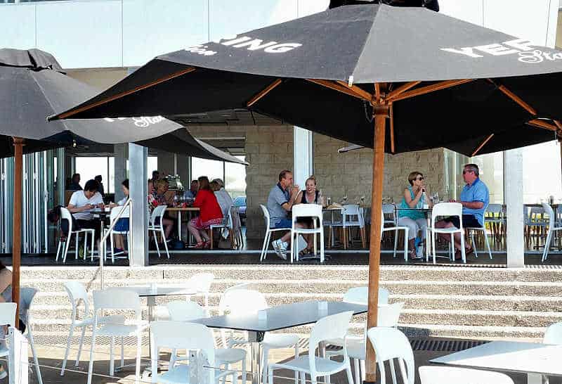 People enjoying al fresco dining at 360Q Restaurant Queenscliff with tables and open umbrella in the foreground.