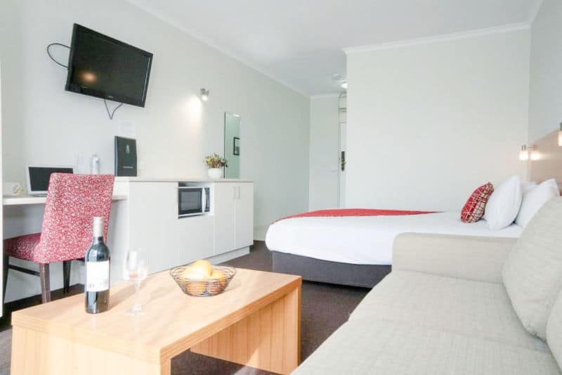 Guest room with bed, couch, and table with a wine bottle at Admiralty Motel in Geelong.