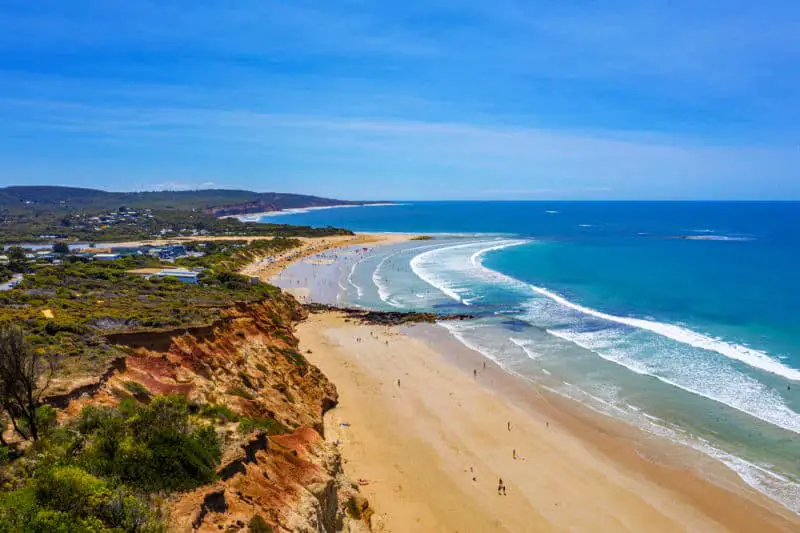 View of Anglesea beach with blue water, golden sand and rugged cliffs.