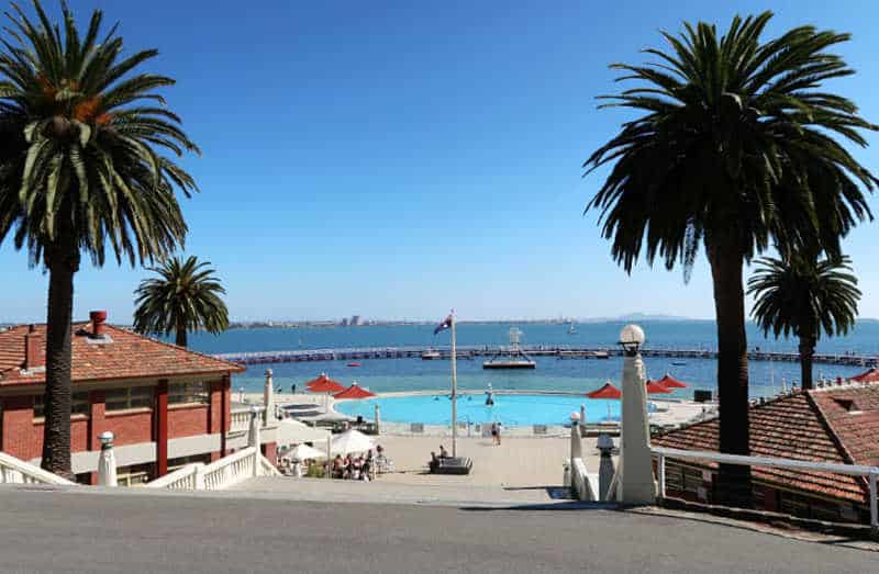 Photo of Eastern Beach children's pool, with the promenade, Australian flag, stairs, and palm trees.