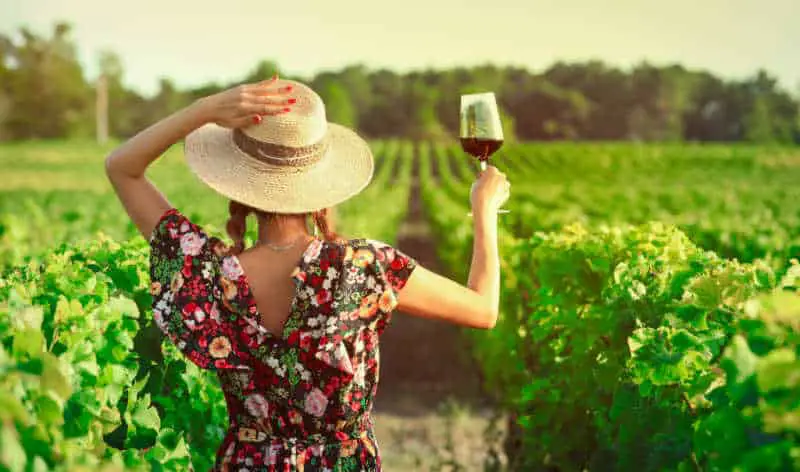 Woman standing amongst the vines holding on to her hat with a glass of wine enjoying one of the great Geelong Winery Tours