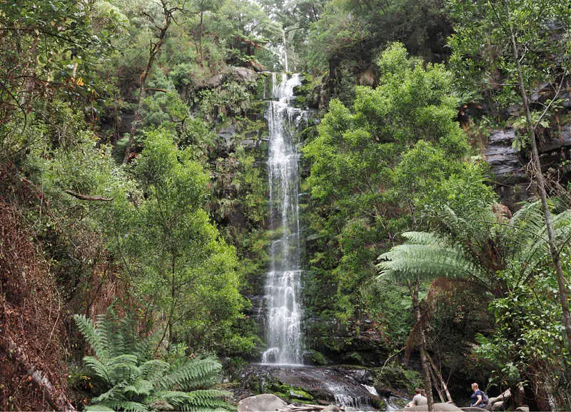 People sitting at the base at one of the cascading GOR waterfalls surrounded by trees and ferns.