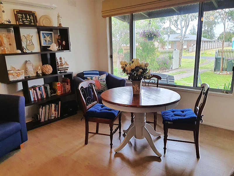 Table and chairs and a bookcase sitting in the window at Little Port Cottage at Portarlington Australia.