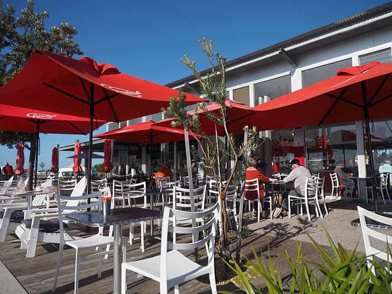 Outdoor dining at one of the Queenscliff restaurants on the harbour with white tables, red umbrellas at blue sky.