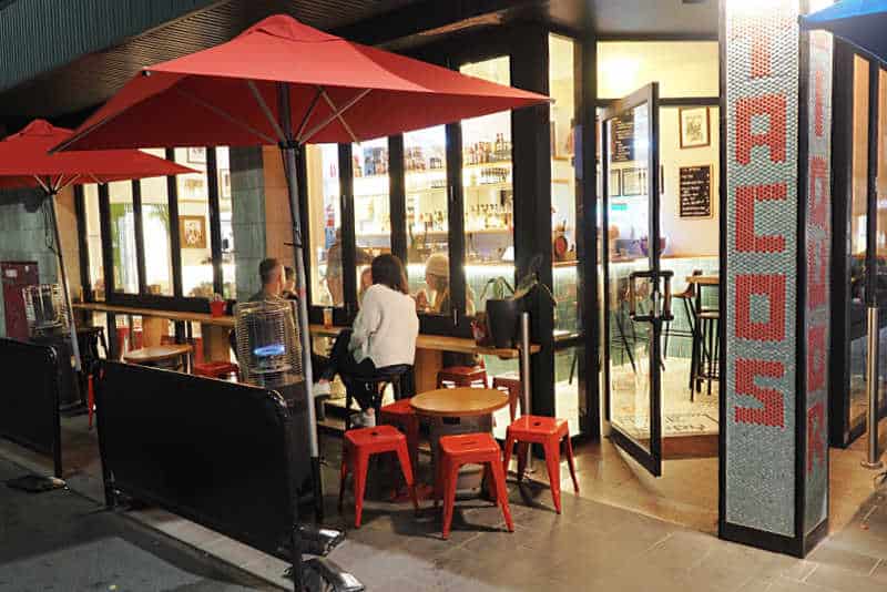 People dining outdoor under a red umbrella at Tacos Y Liquor one of the popular Little Malop Street restaurants.