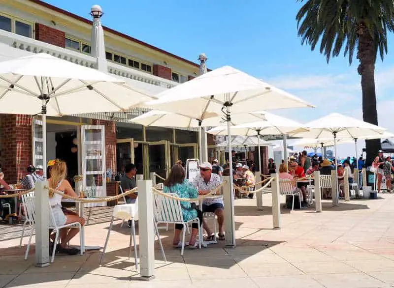 People dining outside under umbrellas at The Beach House Cafe on Eastern Beach Geelong Waterfront..