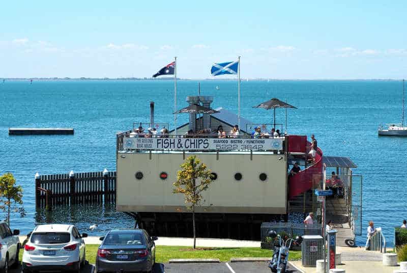 Photo of The Geelong Boat House with flags flying and Corio Bay in the background.